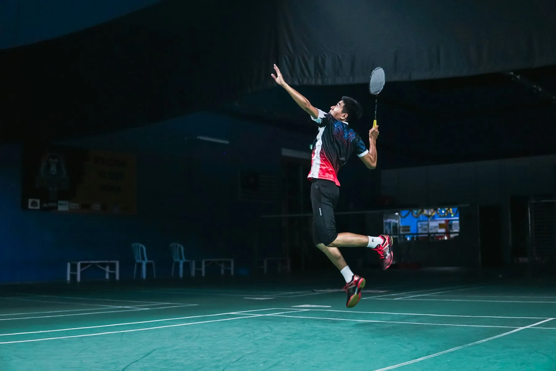 A badminton player leaping into an overhead smash on a floodlit indoor court