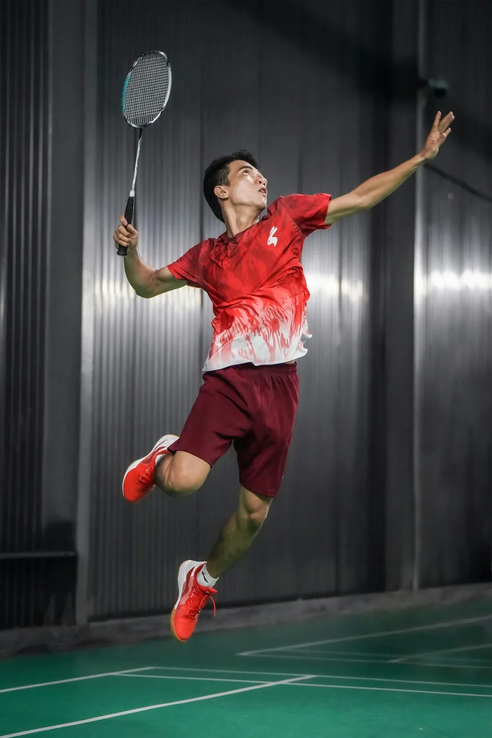 A badminton player rising for an overhead smash on an indoor court
