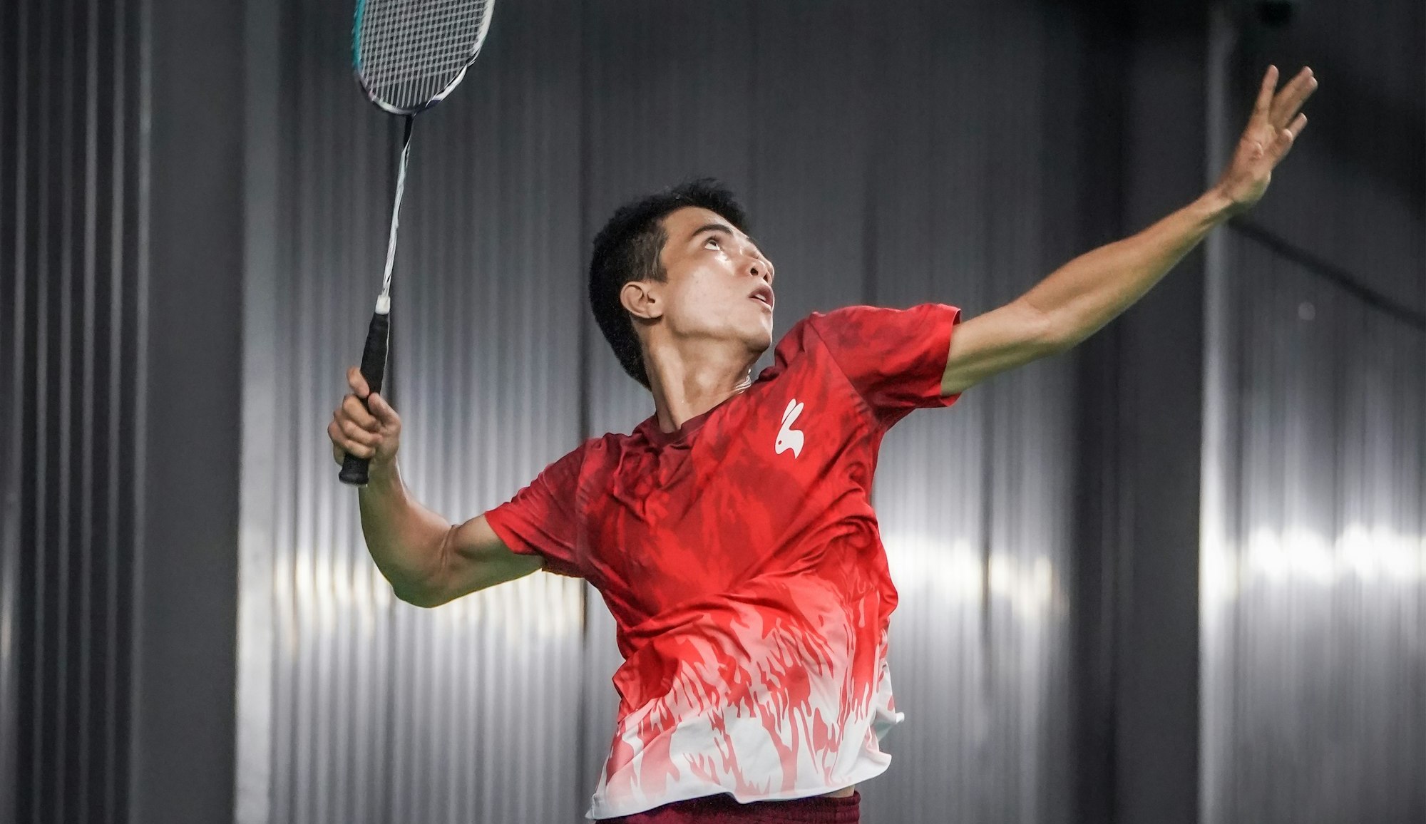 A player reaching high into an overhead smash on an indoor court