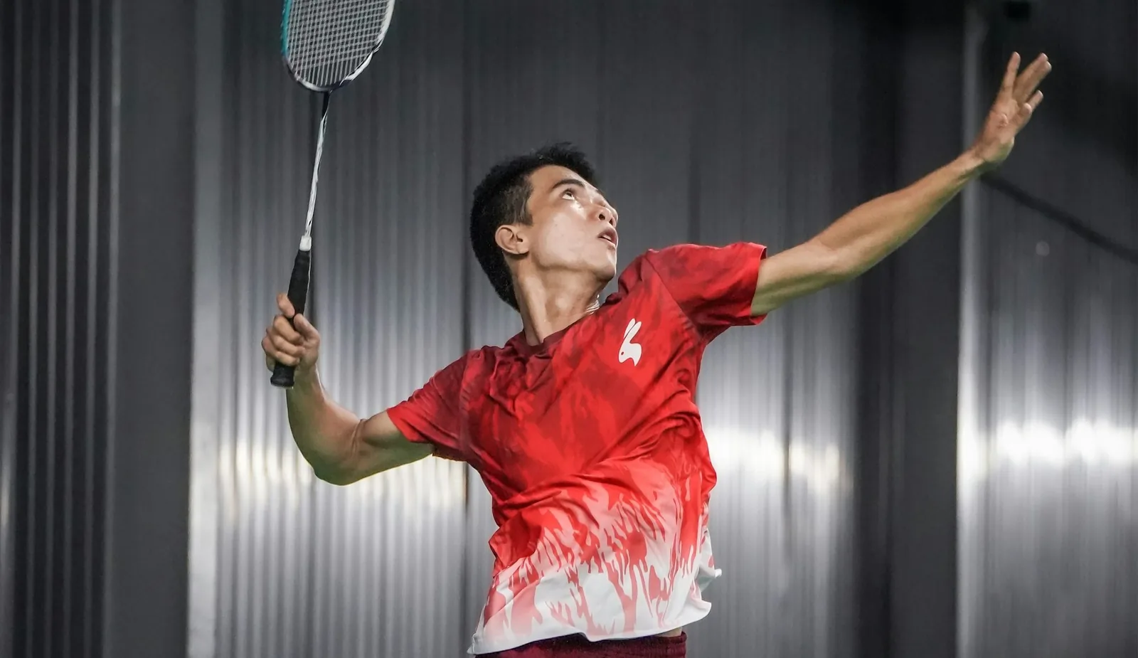A player reaching high into an overhead smash on an indoor court